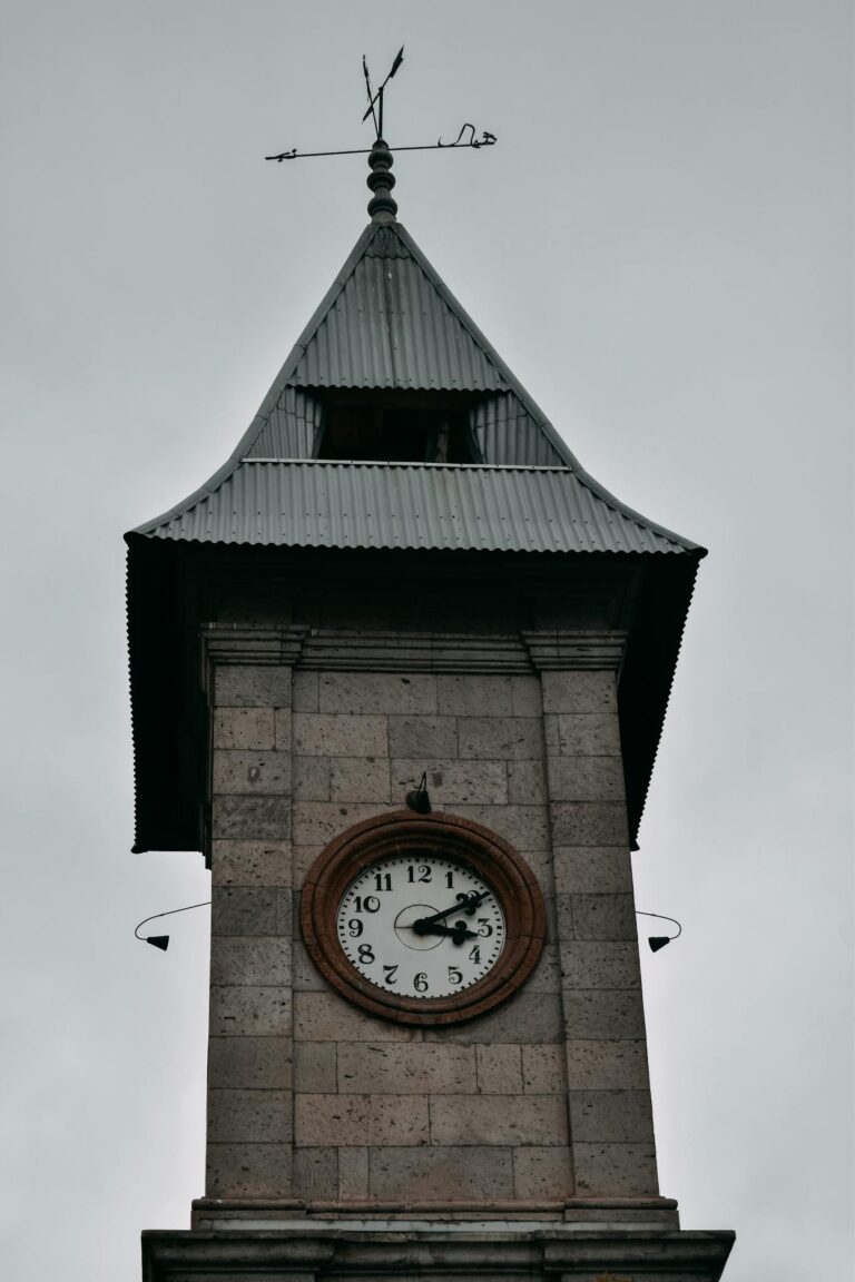 A historic brick clock tower with a weather vane against an overcast sky, showcasing architectural elegance.