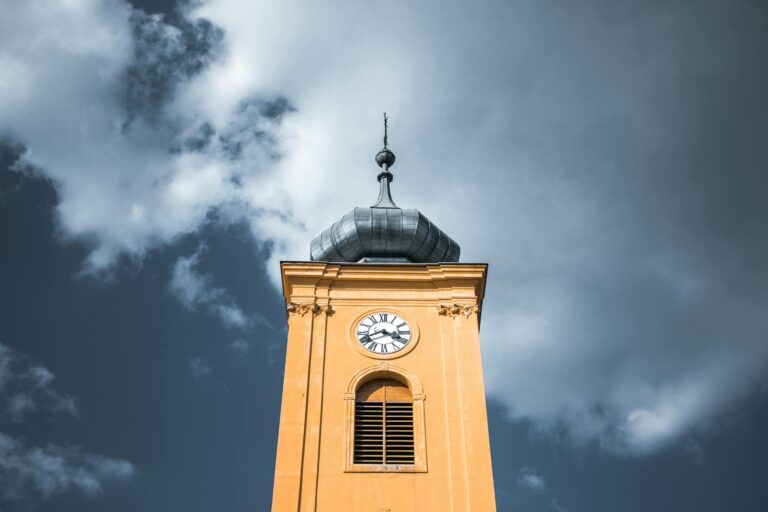 A low-angle view of a historic clock tower with a baroque design against a dramatic cloudy sky in Osijek, Croatia.