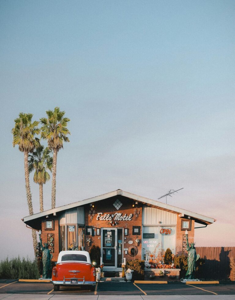 Charming vintage motel facade with palm trees and classic red car under a clear blue sky.