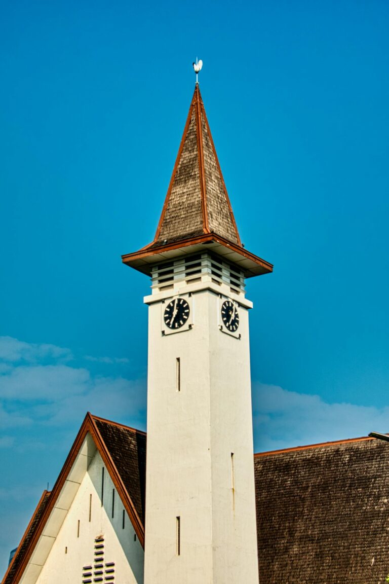 Elegant historic clock tower with pointed roof under a clear blue sky in Jakarta, Indonesia.
